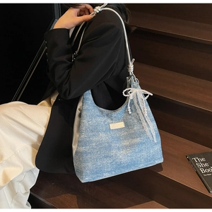 Détail du sac hobo en denim bleu clair avec charm nœud en dentelle et perles
