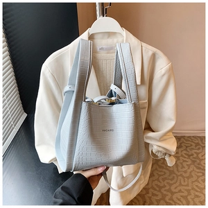 Detail of light blue crocodile pattern handbag with letter branding on white blazer