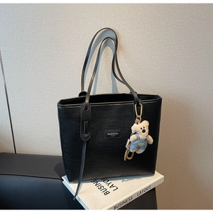 Detail of black woven tote bag with a cute bear charm on a business book background