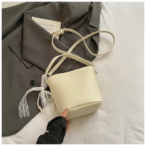 Detail of beige bucket bag with lychee leather texture and pearl lace charm