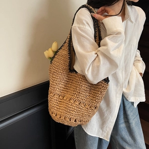 Detail of a beige woven straw tote bag with black straps worn by a model in a casual outfit