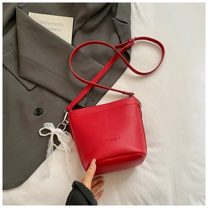 Detail of red pebbled leather bucket bag with lace bow and pearl charm on a grey suit