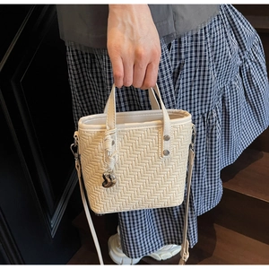 Dettaglio borsa a secchiello intrecciata bianco crema con ciondolo a cuore e tracolla
