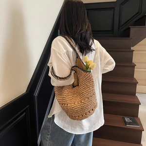 Detailed shot of large woven straw tote bag with black trim on woman's shoulder