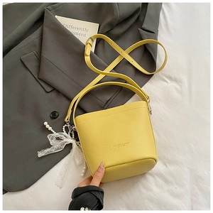 Detail of yellow pebbled leather bucket bag featuring lace bow and pearl pendant charm