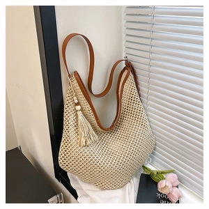 Detail der beige geflochtenen Strohtasche mit braunem Lederriemen und Quasten-Akzent