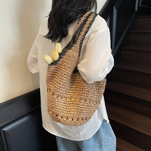 Close-up of a woven straw tote bag with black trim accents and a fresh tulip decoration