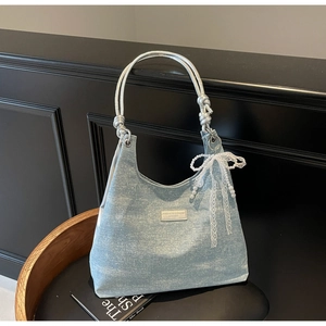 Gros plan du sac en denim bleu clair avec poignée en corde argentée et nœud en perles