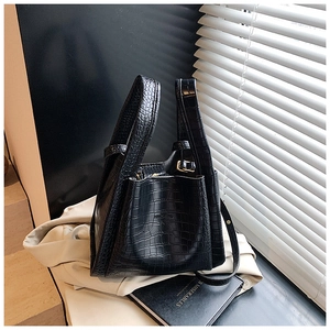 Macro shot of black crocodile-embossed leather texture and gold hardware on bucket bag