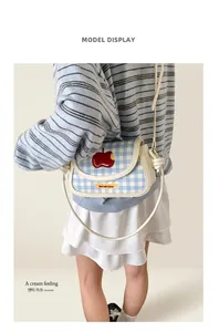 Detail of blue plaid crossbody bag with apple embroidery shown on a female model