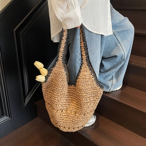 Close-up of a woven straw tote bag with black trim held on wooden steps in a casual scene