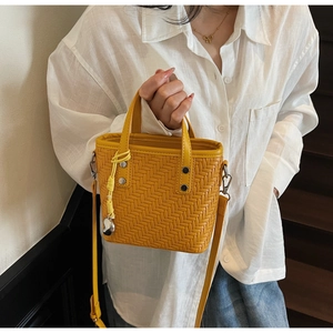 Dettaglio di una borsa a secchiello gialla intrecciata con ciondolo a cuore e tracolla