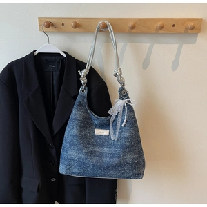 Vue détaillée du sac sous le bras en jean avec sangle argentée et nœud sur un blazer