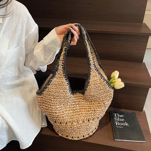 Detail of straw woven tote bag featuring black contrast trim and V-shaped handle design