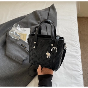Dettaglio borsa shopper nera intrecciata con ciondolo a cuore argento e tracolla su letto