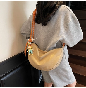 Detalle del bolso bandolera media luna caqui con correa tejida y colgante en el modelo