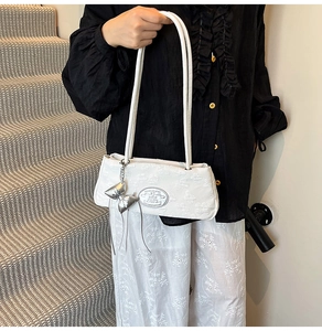 Dettaglio borsa sottobraccio bianca goffrata con ciondolo a fiocco e logo metallico