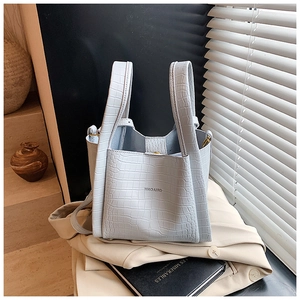 Close-up of light blue crocodile texture bucket bag on a beige blazer background