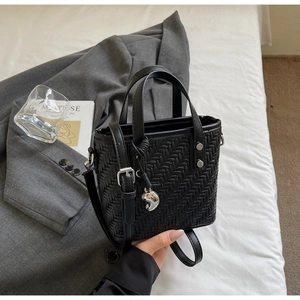 Dettaglio borsa a mano in pelle intrecciata nera con ciondolo a cuore e tracolla regolabile