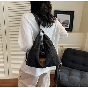Close-up of black canvas tote bag showing the brown leather logo and metal buckle detail