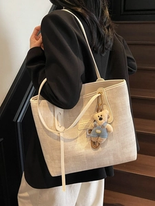 Minimalist beige woven tote bag with leather trim and bear pendant on a shoulder model