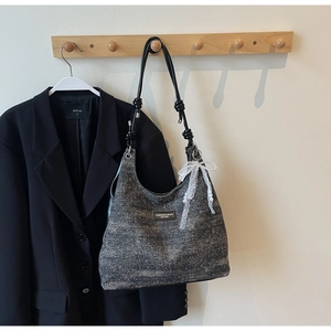 Détail d'un sac à bandoulière gris scintillant avec nœud en dentelle et plaque en métal