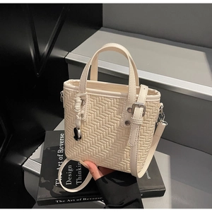 Dettaglio mini borsa tote color crema intrecciata con tracolla e ciondolo in metallo