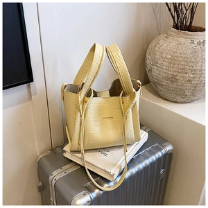 Close-up of a pale yellow crocodile embossed handbag with thin strap and HMOAIRD logo