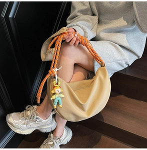 Detalle de bolso bandolera beige media luna con correa de cuerda naranja y colgante de dibujo