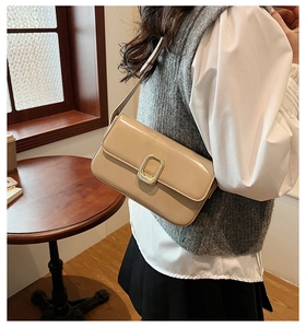 Detalle de un bolso de hombro beige brillante con hebilla metálica rectangular dorada