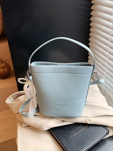 Stylish light blue leather bucket bag with top handle and pearl lace charm on blazer