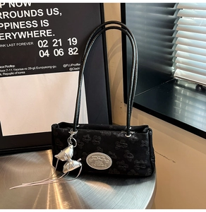 Dettaglio borsa a spalla in nylon nero a fiori con ciondolo a fiocco argento su scrivania