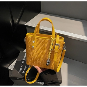 Dettaglio borsa a secchiello intrecciata giallo vivace con ciondolo a cuore su sfondo moderno