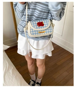Close-up of blue plaid crossbody bag with red apple patch and adjustable strap details
