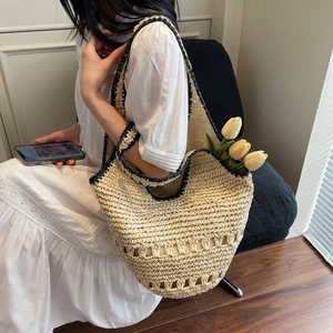 Detail of a woven straw tote bag featuring black contrast trim and hollow weave pattern