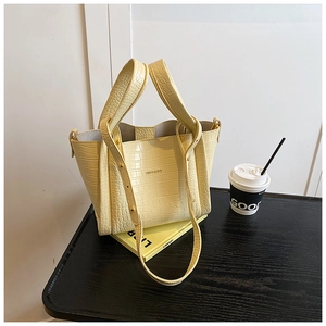 Detail shot of a yellow croc-embossed bucket bag with metallic logo and detachable strap