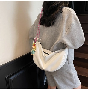 Detalle de bolso bandolera blanco en forma de media luna con correa de colores y amuleto