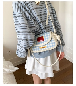 Detail of blue and white checkered crossbody bag with red apple patch on striped sweater