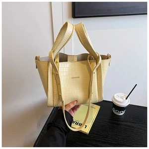 Detail of cream yellow crocodile embossed tote bag with dual handles on wooden surface