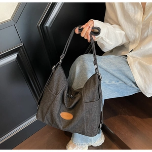 Detail of grey denim hobo bag with adjustable strap and orange logo on model