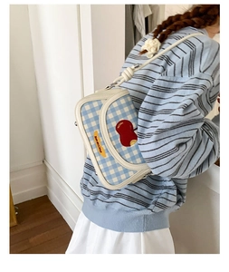 Detail of blue plaid square crossbody bag featuring apple embroidery and knotted strap