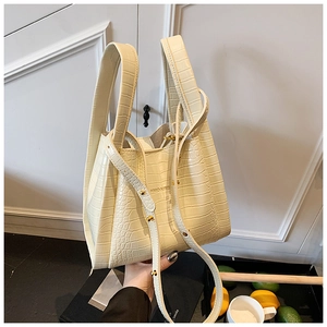 Detail of off-white crocodile pattern handbag featuring gold rivets and shoulder strap