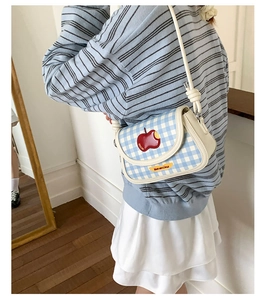 Detail of blue plaid saddle bag with red apple embroidery and Not Anxious label