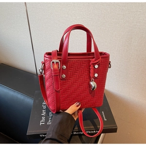 Dettaglio borsa a secchiello rossa intrecciata con ciondolo a cuore e tracolla regolabile