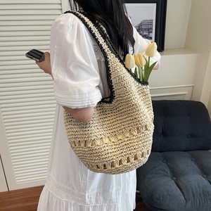 Detail of large woven straw tote bag with black trim and hollowed patterns on side
