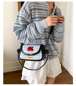 Detail of checkered crossbody bag featuring a red apple patch and Not Anxious strap text