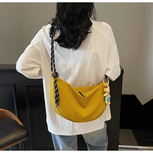 Detalle de bolso medialuna de lona amarilla con correa de cuerda tejida y colgante de peluche