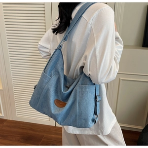 Detail of blue denim tote bag with brown leather patch and adjustable shoulder strap