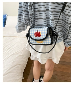 Detail of blue plaid crossbody bag with apple embroidery and 'Not anxious' text label