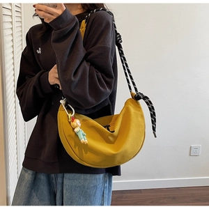 Detalle de bolso luna de lona amarilla con correa tejida y colgante de colores